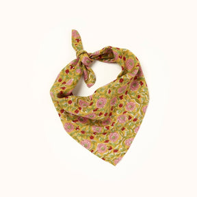 A red, pink, green and yellow floral patterned bandana. folded over and tied in a knot. Block printed by hand, the Maya Bandana from Maelu is designed in Portland, Oregon and handmade in India.