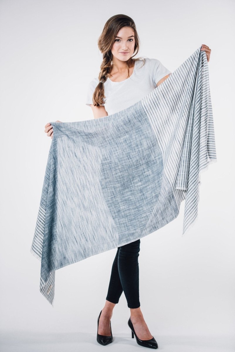 Model holds up a blue scarf with white stripes and cotton fringe. The Malabar Natural Khadi Scarf in Blue is from Bloom & Give and hand-loomed in South India.