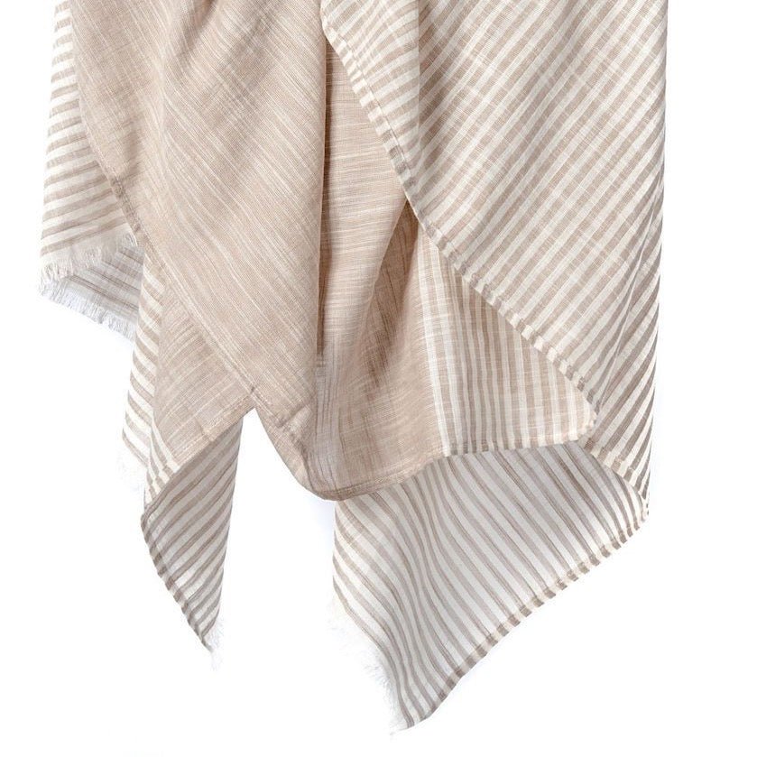 Natural cotton scarf with white stripes and cotton fringe hangs in the air. The Malabar Natural Khadi Scarf is from Bloom & Give and hand-loomed in South India.