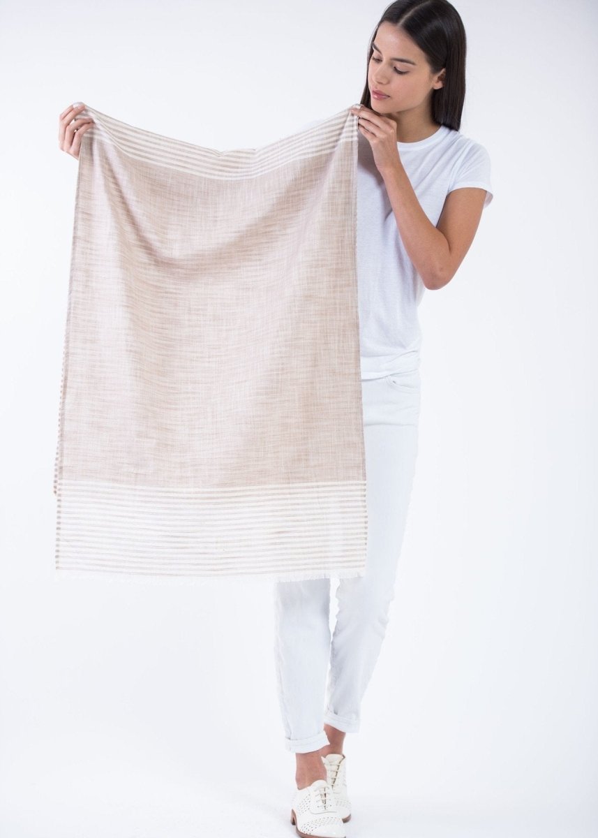 Model holds up the Malabar Natural Khadi Scarf with white stripes and cotton fringe. This natural cotton scarf is from Boom & Give and hand-loomed in South India.
