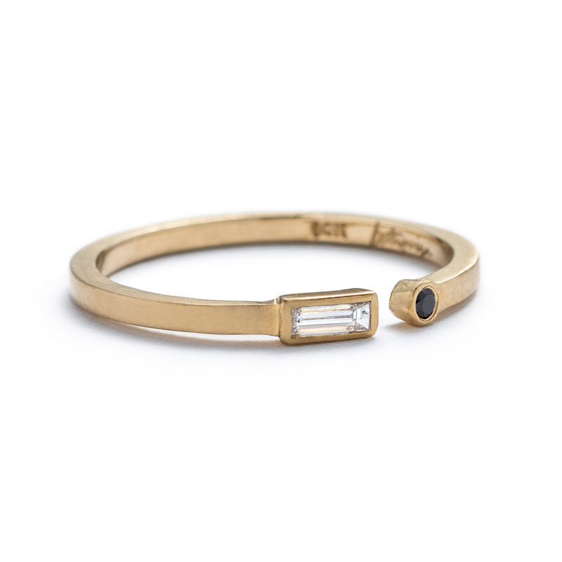Thin, 14k yellow gold adjustable ring with a matte finish, bezel-set with a small, white diamond baguette on one end, and a small, round, black diamond on the opposite end, with the betsy & iya logo engraved inside the band. Hand-crafted in Portland, Oregon. 