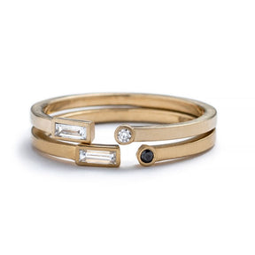 A pair of 14k yellow gold betsy & iya Manus Rings, with small, white diamond baguettes and small, round, white and black diamonds bezel-set on opposite ends. Hand-crafted in Portland, Oregon.