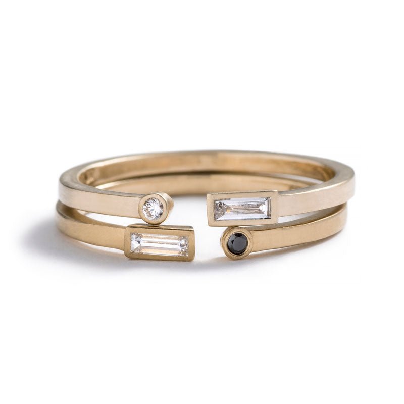A pair of 14k yellow gold betsy & iya Manus Rings, with small, white diamond baguettes and small, round, white and black diamonds bezel-set on opposite ends. Hand-crafted in Portland, Oregon.