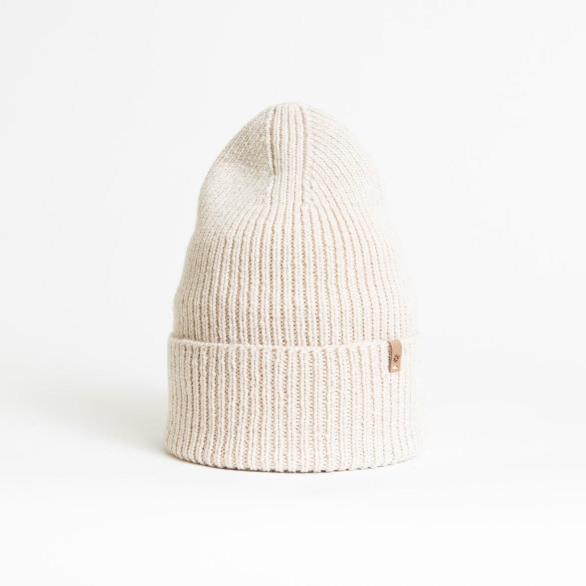 A warm cream colored knitted and cuffed hat with a decrease detail on top. The Merino Rib Hat in Almond White is designed by Dinadi and hand knitted in Kathmandu, Nepal.