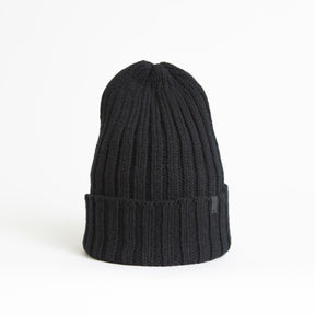 A black cuffed hat with thick ribbed design and decrease detail at the top. The Merino Thick Rib Hat in Black is designed by Dinadi and hand knitted in Kathmandu, Nepal.