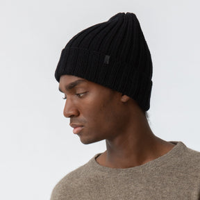 A black cuffed hat with thick ribbed design and decrease detail at the top. The Merino Thick Rib Hat in Black is designed by Dinadi and hand knitted in Kathmandu, Nepal.