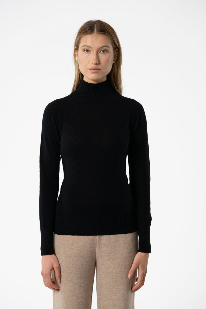 A model wears a long sleeve knitted mock neck turtleneck in black. The Merino Turtleneck in Black is designed by Dinadi and hand knitted in Kathmandu, Nepal.