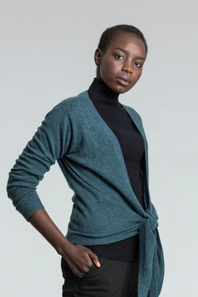 Model shows blue/green knitted wrap cardigan tied loosely in front. The Merino Wrap Cardigan in Dragonfly Green in designed by Dinadi and made in Kathmandu, Nepal.