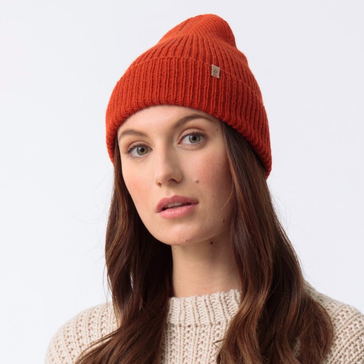 Bright orange knitted and cuffed hat with a decrease detail on top. The Merino Rib hat in Burnt Orange is designed by Dinadi and hand knitted in Kathmandu, Nepal.