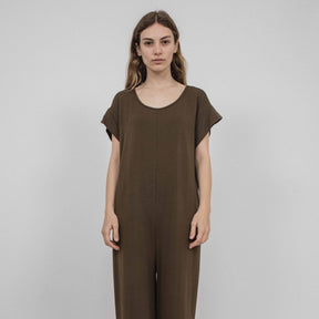 A model wears a crewneck short sleeve jumpsuit in a rich brown. It has a cuffed sleeve detail and is easy to take on and off. The Miriam Jumpsuit in mocha is designed and made by Corinne Collection in Los Angeles, CA.