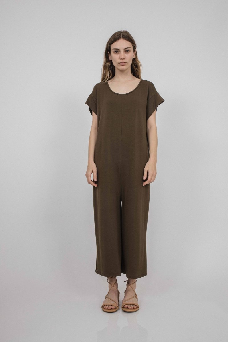 A model wears a crewneck short sleeve jumpsuit in a rich brown. It has a cuffed sleeve detail and is easy to take on and off. The Miriam Jumpsuit in mocha is designed and made by Corinne Collection in Los Angeles, CA.