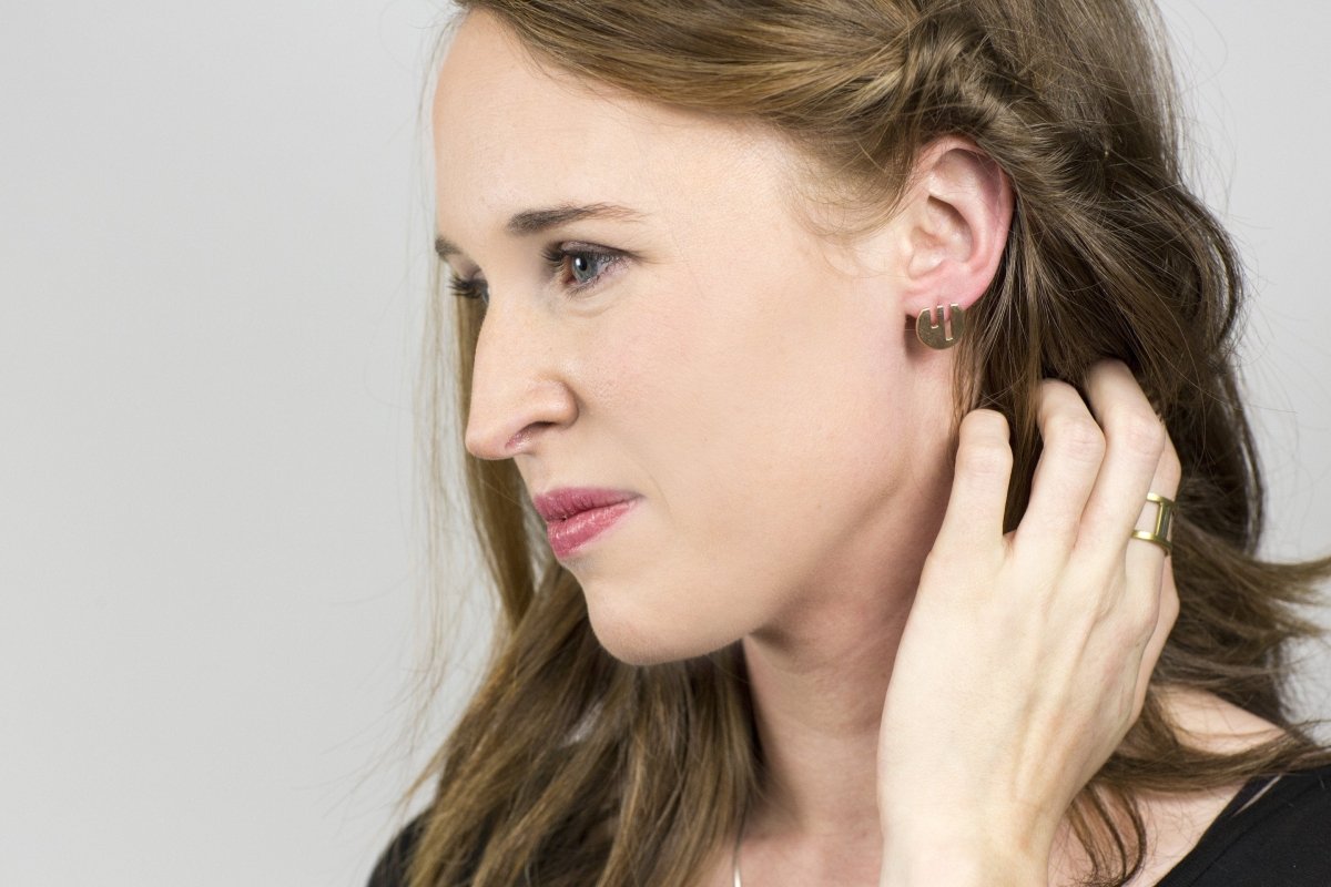 The circular betsy & iya Vous et Moi bronze stud, pictured on the profile of a model with long, straight hair. 