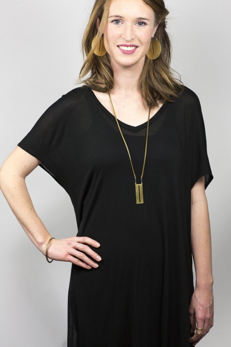 Long, geometric, brass La Luz statement necklace, worn by a smiling model with betsy & iya large brass Lié hoop earrings.