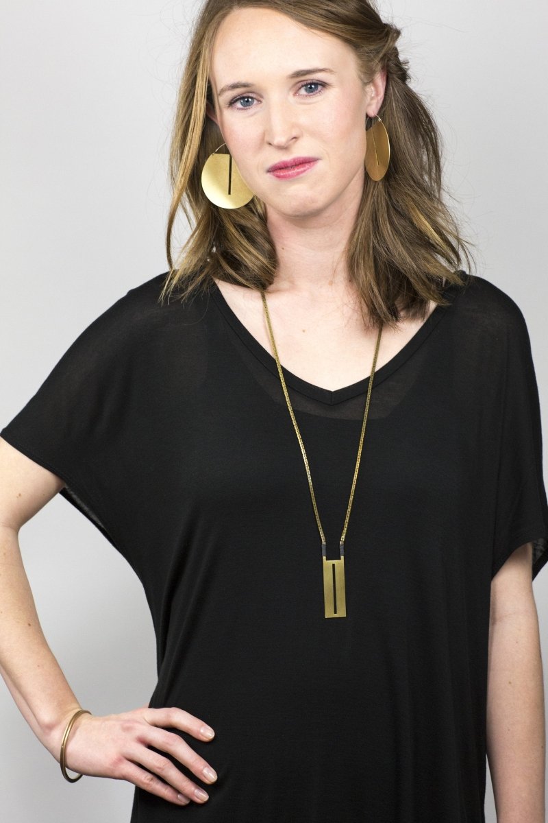 Eye-catching, large betsy & iya Lié hoop earrings, styled on a model with a brass betsy & iya La Luz geometric statement necklace. 