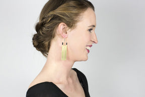Rectangular brass earrings with thin slit cutouts down the center, accented with gray Japanese cotton thread and sterling silver earring wires, shown on the profile of a smiling model.