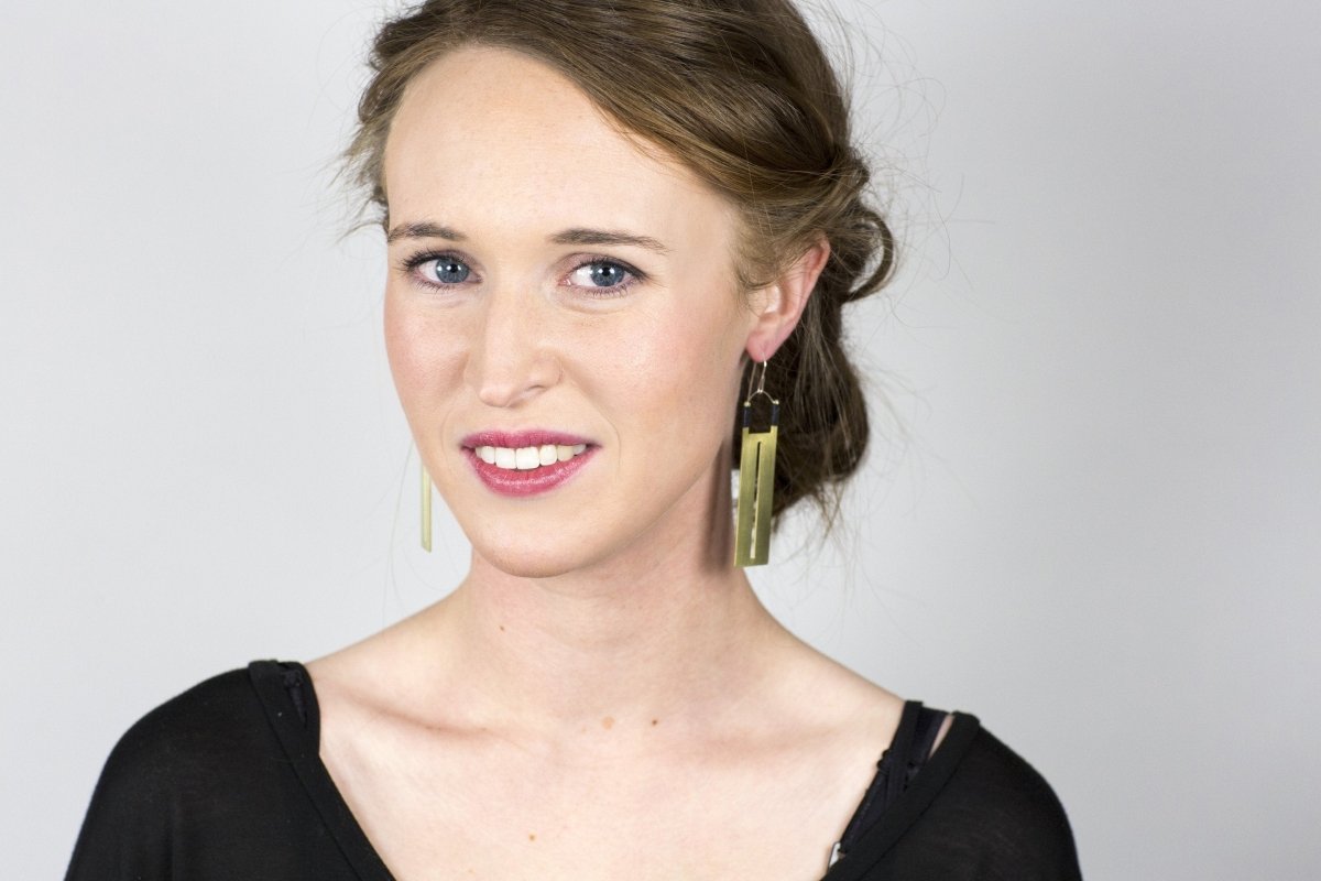Rectangular brass earrings with thin slit cutouts down the center, accented with gray Japanese cotton thread and sterling silver earring wires, worn by a smiling model with an updo.