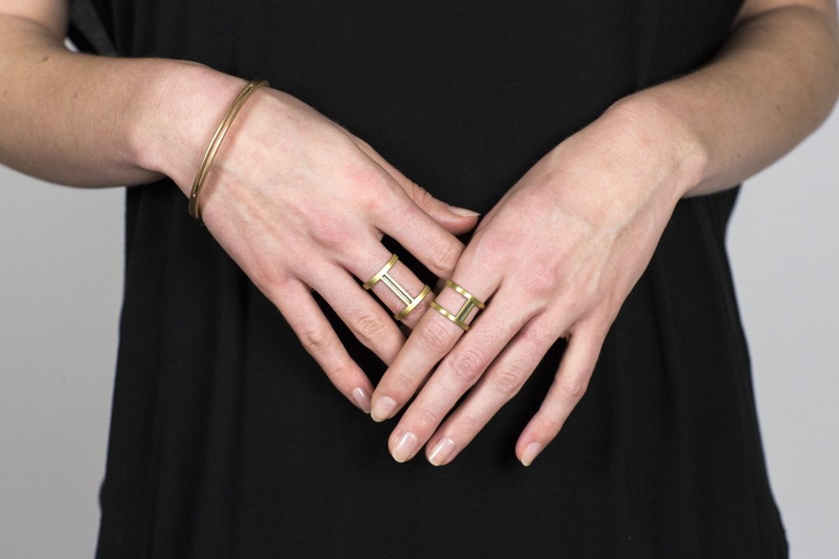 One short, brass Nous ring, and one long, brass Nous ring, worn on either hand of a model, and accented with a betsy & iya bronze Juntos bangle.