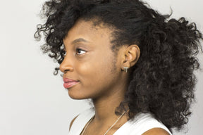 The t-shaped Vous et Moi silver stud, pictured on the profile of a smiling model with curly hair and a white top.