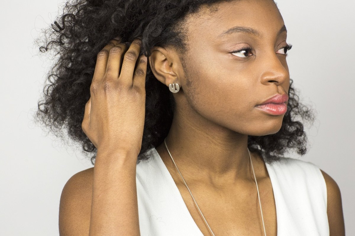 The circular Vous et Moi silver stud, pictured on the profile of a model with curly hair and a white top.