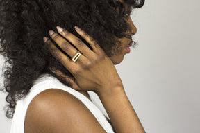 A bronze betsy & iya Mía ring, worn alone by a model with curly hair and a white outfit.