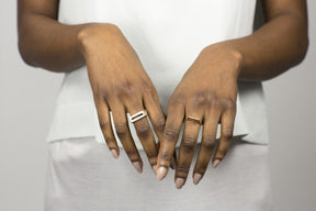 A close-up shot of a model's hands, featuring a bronze betsy & iya Tuyo ring on one hand, and a silver betsy & iya Mía ring on the other.