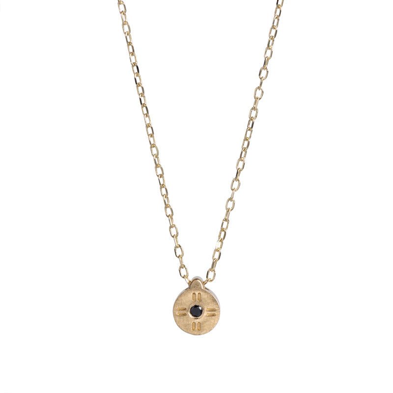 Tiny, circular pendant of 14k yellow gold, with subtle engraved details around a small black diamond, on a 14k gold chain. Hand-crafted in Portland, Oregon. 