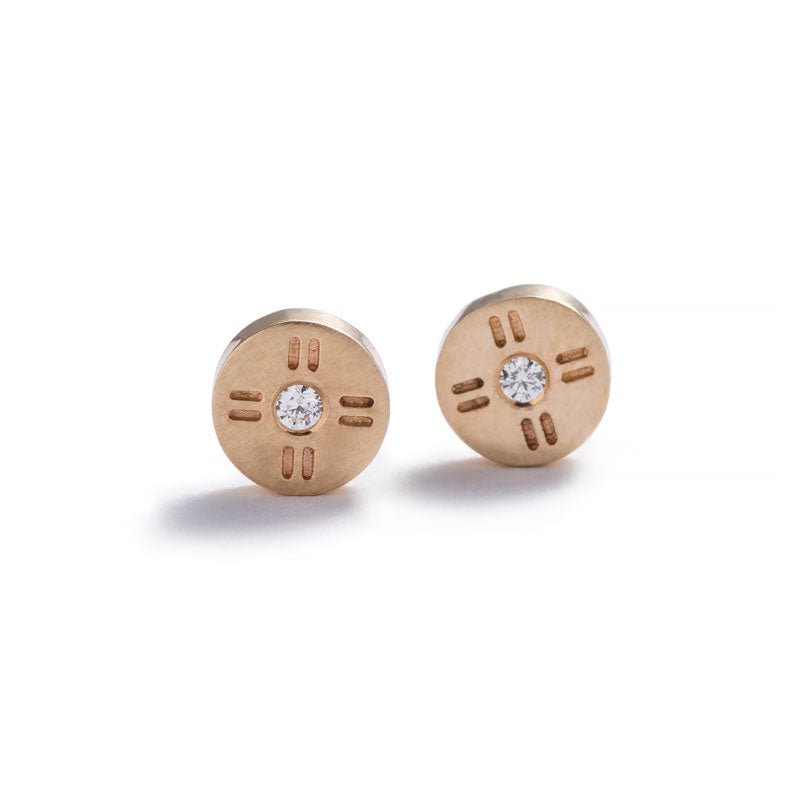 Tiny, circular stud earrings of 14k yellow gold, with subtle engraved details around a round, white diamond. Hand-crafted in Portland, Oregon.