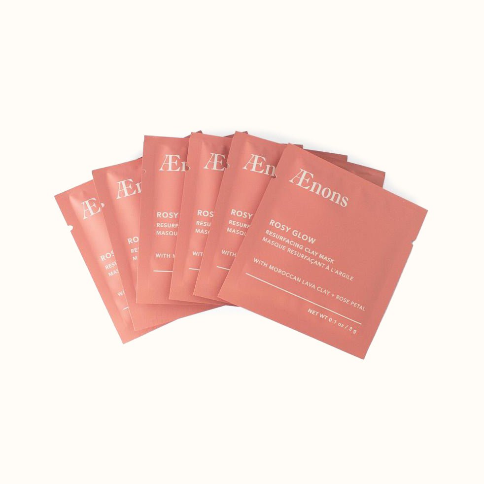 A fan of small pink packages against a white background. The Rose Glow Resurfacing Clay Mask with Moroccan Lava Clay + Rose Petal is crafted by Aenons and made in Los Angeles, CA.