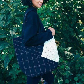 Model wears black tote with white cross-stitching and color-blocked design. Designed by Anchal in Louisville, Kentucky and handmade in Ajmer, India.