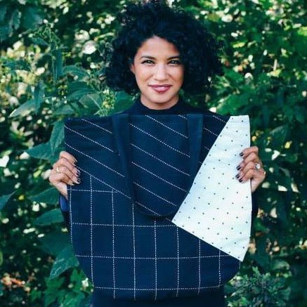 Model holds up black tote with white cross-stitching and color-blocked design. Designed by Anchal in Louisville, Kentucky and handmade in Ajmer, India.