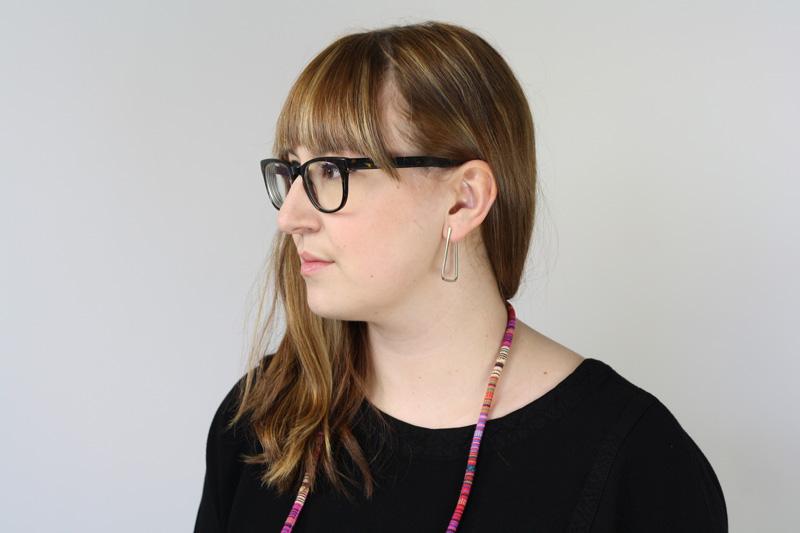 Simple, elegant Nama hoop earrings in silver, pictured on the profile of a model wearing glasses and a retired betsy & iya colorful statement necklace.