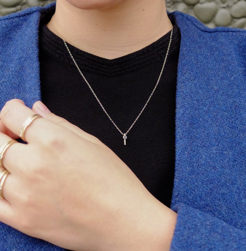Small, ankh-shaped 14k yellow gold pendant with a black diamond and delicate gold chain, styled on a model with a black shirt and blue sweater.
