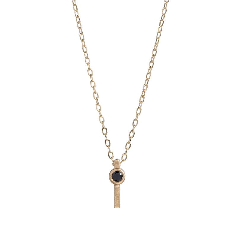Tiny, ankh-shaped pendant of 14k yellow gold, topped with a round, bezel-set black diamond, and threaded with a delicate gold chain. Hand-crafted in Portland, Oregon.