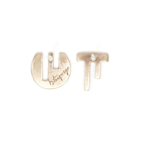 A pair of mismatched, bronze stud earrings, with complementary geometric cutouts that fit into one another like puzzle pieces, and the betsy & iya logo engraved on the back of the circular stud. Hand-crafted in Portland, Oregon.