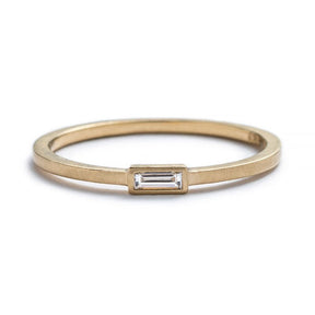 Thin, 14k yellow gold ring with a matte finish and a small, white diamond baguette bezel-set parallel to the band. Hand-crafted in Portland, Oregon. 