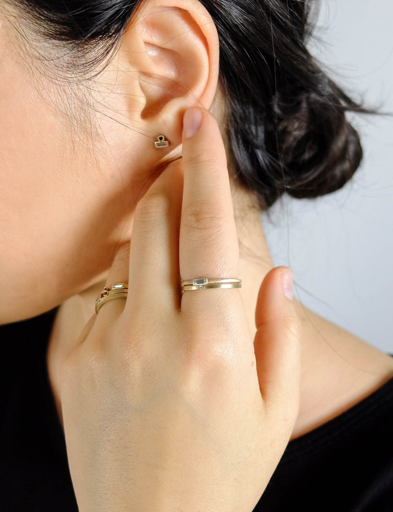 White diamond and 14k yellow gold Nitor and Vis rings, pictured on a model wearing a black shirt and betsy & iya 14k yellow gold and black diamond Ipsum stud earrings.