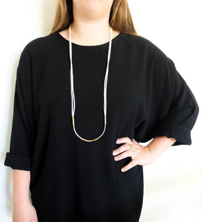 Cotton, brass, and sterling silver Ora statement necklace, worn long on a model with a black tunic.