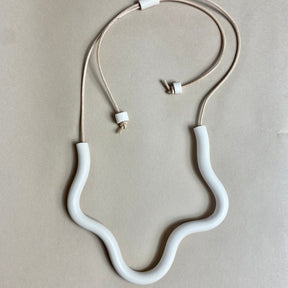 A polymer clay necklace in a wave design with an adjustable leather strap. The Organic Form Necklace in Cream is designed and handcrafted by Little Pieces Jewelry in Los Angeles, California.
