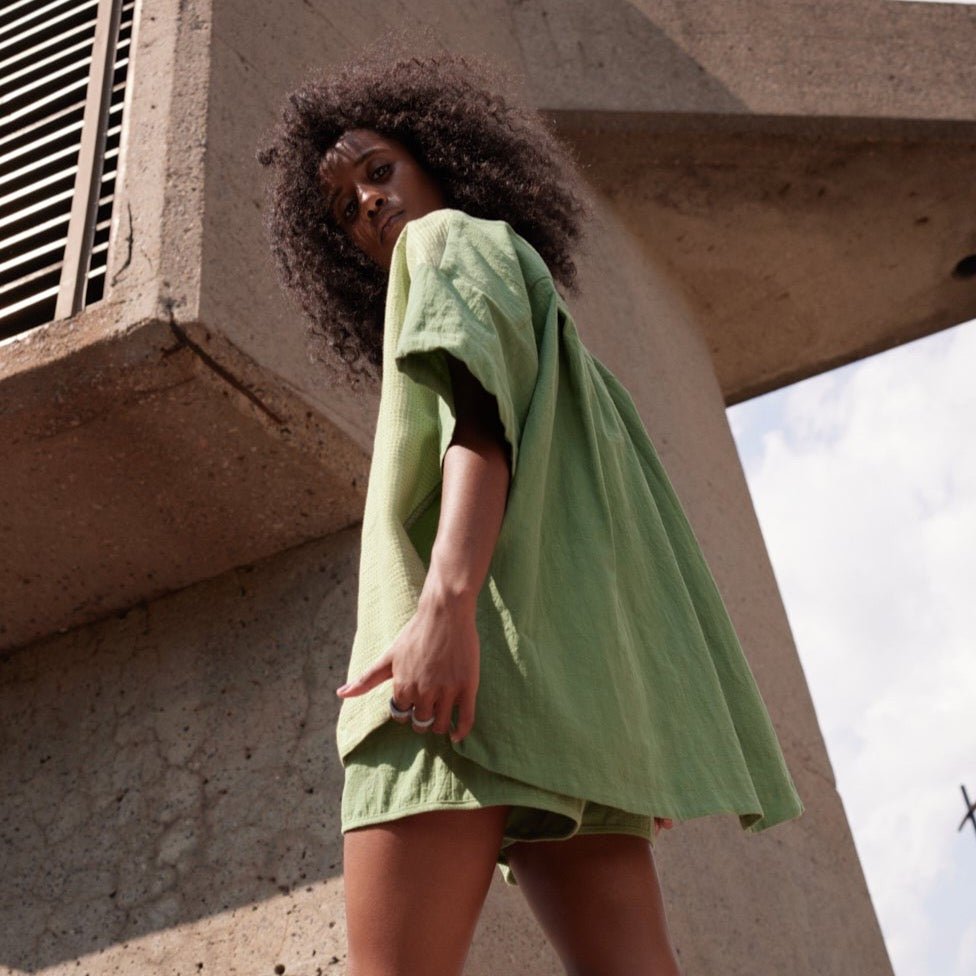 A model shows the back side of a two tone button up in a moss green and a light green with a light green pocket. The Pandora Shirt in Lime & Matcha is designed by Eve Gravel and made in Montreal, Canada.