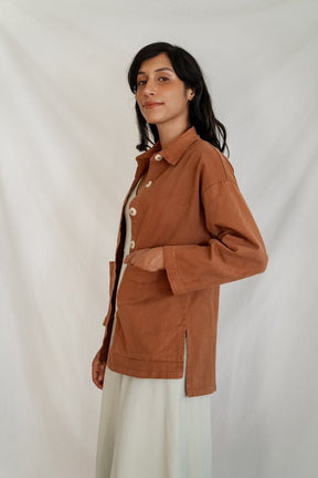 Model shows side profile of a chore jacket with off-white buttons and two oversized pockets in the color Saddle Brown. The Painter's Jacket is designed by Mien and made in Los Angeles, CA.