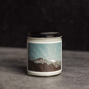Clear glass jar candle with a black lid and mountain landscape artwork. The Peak Jar Candle is hand-poured by Particle Goods in Seattle, WA.