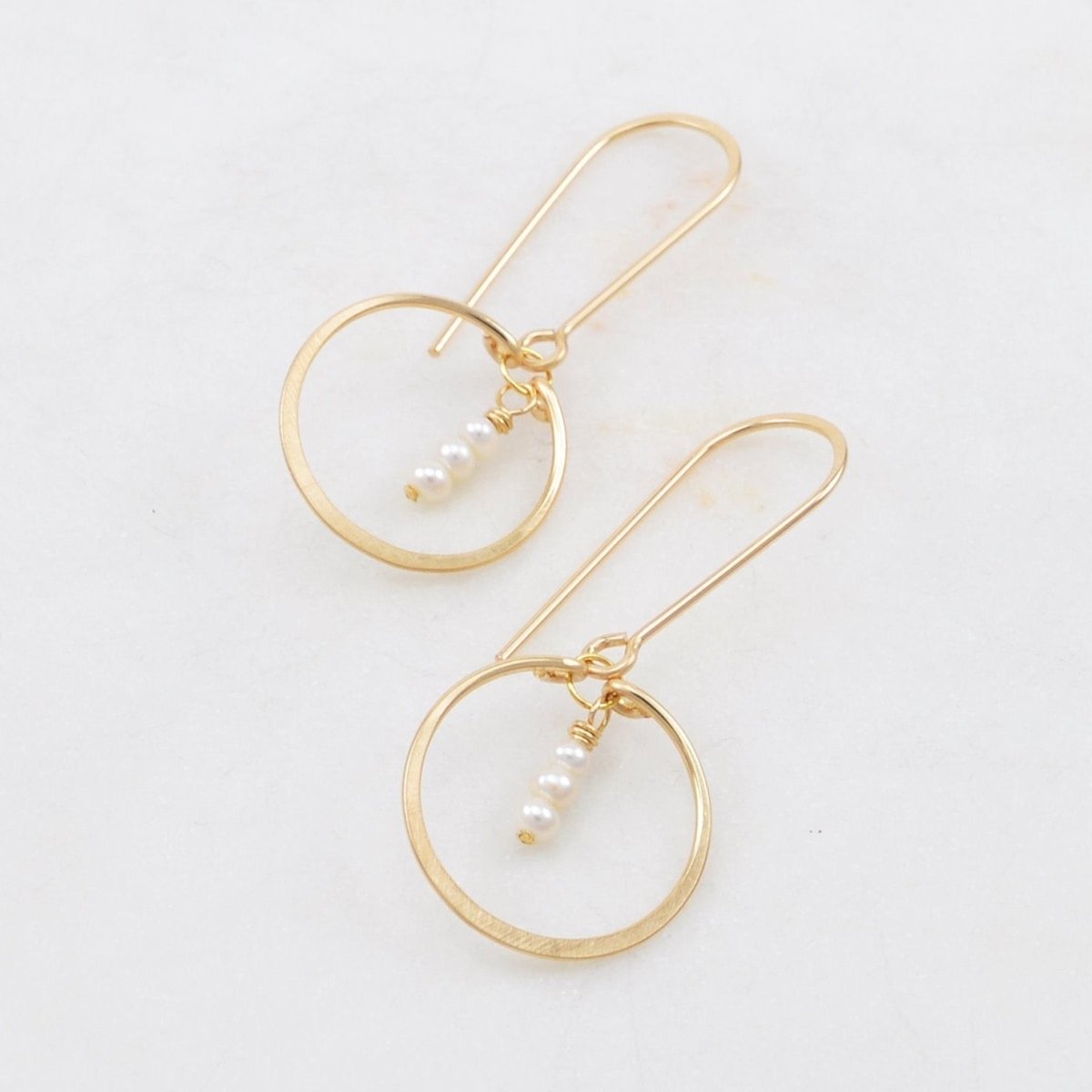 A curved gold-fill ear wire holds a delicate gold-fill hammered circle. Three small freshwater pearls hang in the center of the circle. The Petite Circle Gem Drop Earrings with Fresh Water Pearls are designed and handcrafted by Amy Olson in Portland, Oregon.
