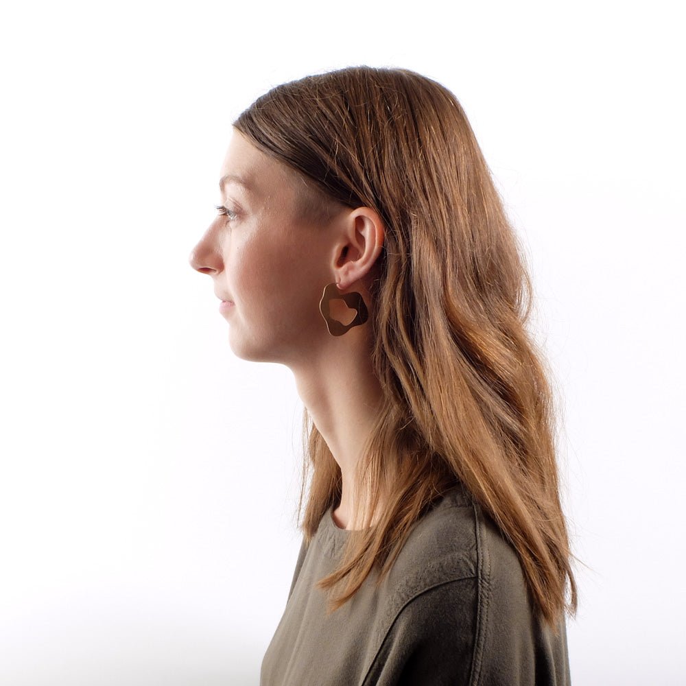 Bronze betsy & iya Renna hoop earrings, pictured on the profile of a model with long, golden brown hair.