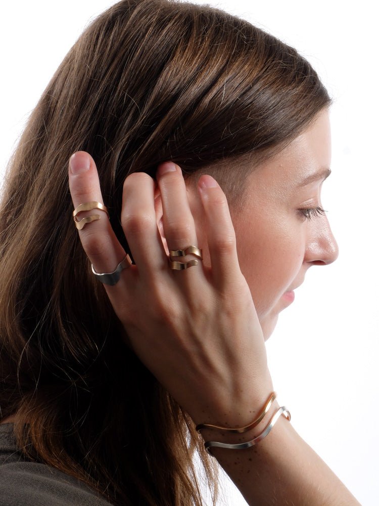 Two bronze, and one sterling silver, Willamette adjustable rings, pictured on a model as she brushes back her hair, and accompanied by one bronze and one silver betsy & iya Fluit cuff bracelet.