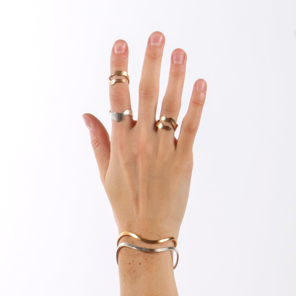 A pair of bronze and sterling silver Fluit cuff bracelets, styled on a model's hand with two bronze and one sterling silver betsy & iya Willamette adjustable rings. 