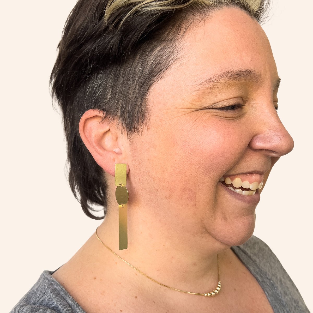 A model wears a long brass earring made with two rectangular pieces interconnected with a single circular shape. Designed and handcrafted in Portland, Oregon.