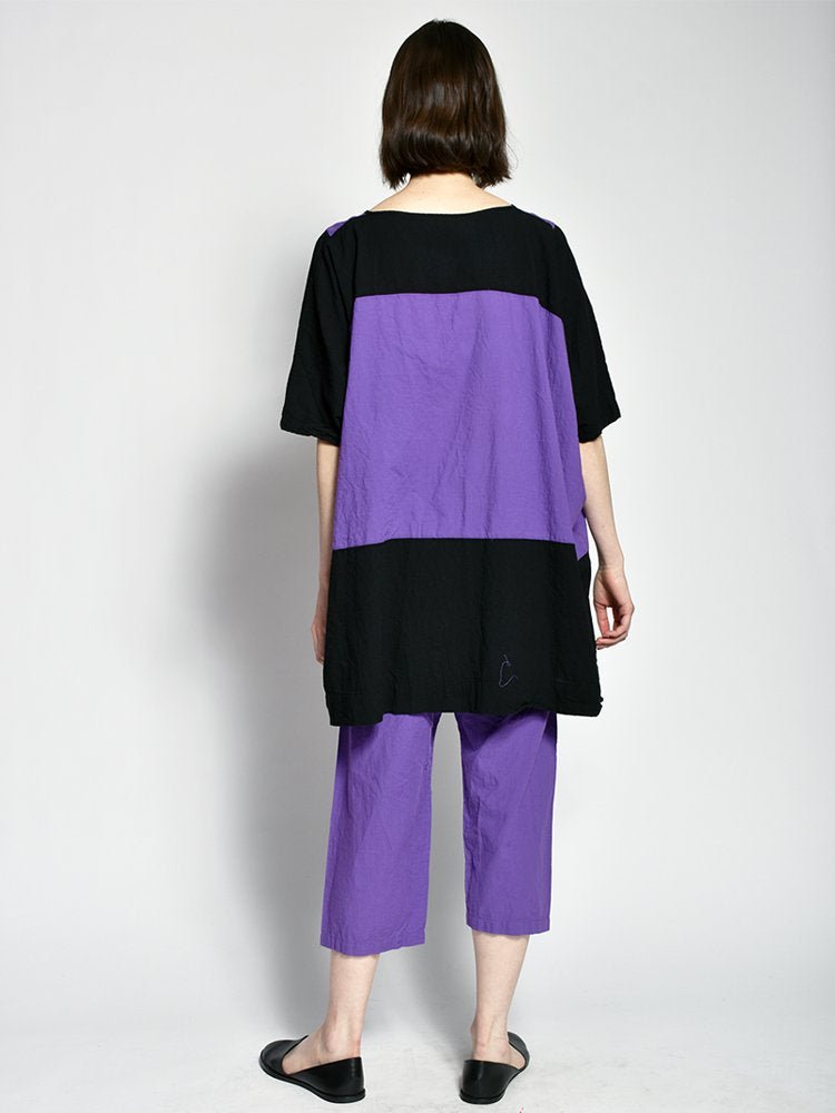 Model shows the backside of a purple and black tunic style dress with a color blocked design. The Triangle Dress in Purple is designed and sewn by Uzi in Brooklyn, New York.