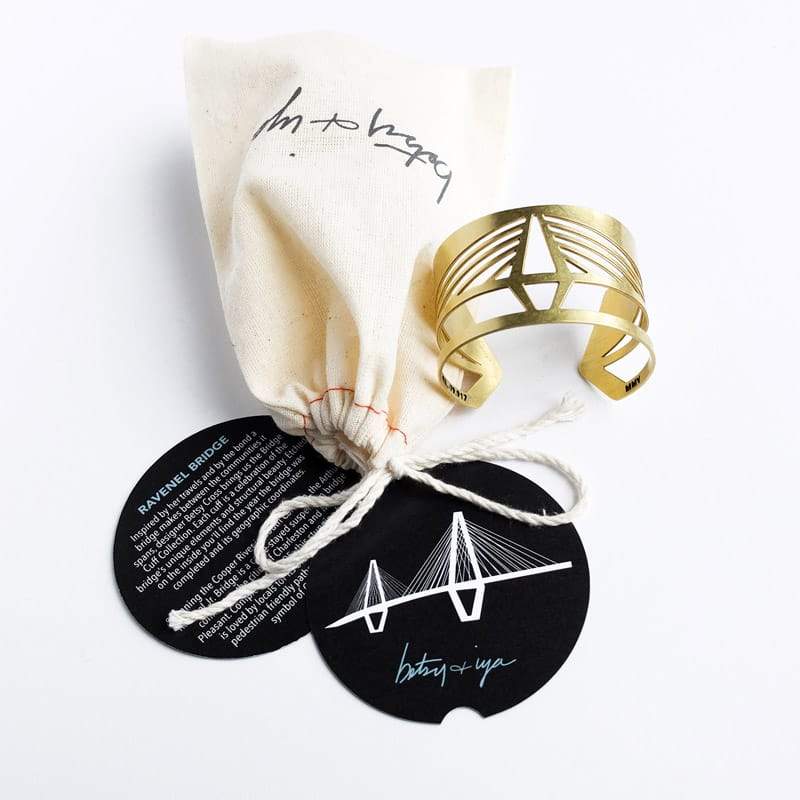 Brass Ravenel cuff bracelet with signature betsy & iya muslin cuff bag and round, informational cards about the Ravenel bridge and cuff bracelet care. Hand-crafted in Portland, Oregon.