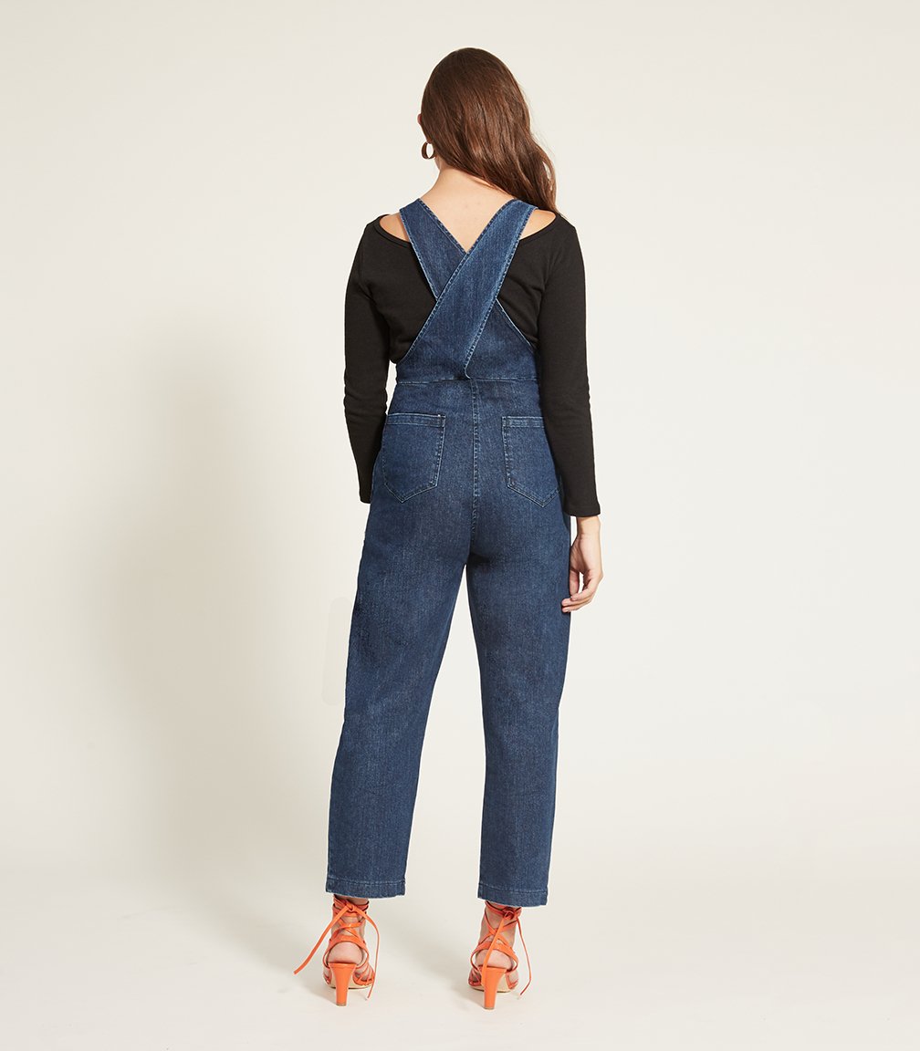 Model shows the back side of the Rhoda Coveralls in Indigo over a black long sleeved shirt. The Rhoda Coveralls in Indigo are designed by Loup and made in New York City, USA.