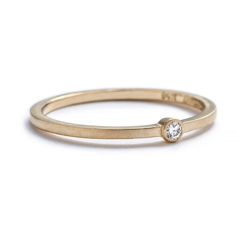 Thin, 14k yellow gold band with a matte finish, featuring a small, round, bezel-set white diamond, and engraved on the inner band with the betsy & iya logo. Hand-crafted in Portland, Oregon. 